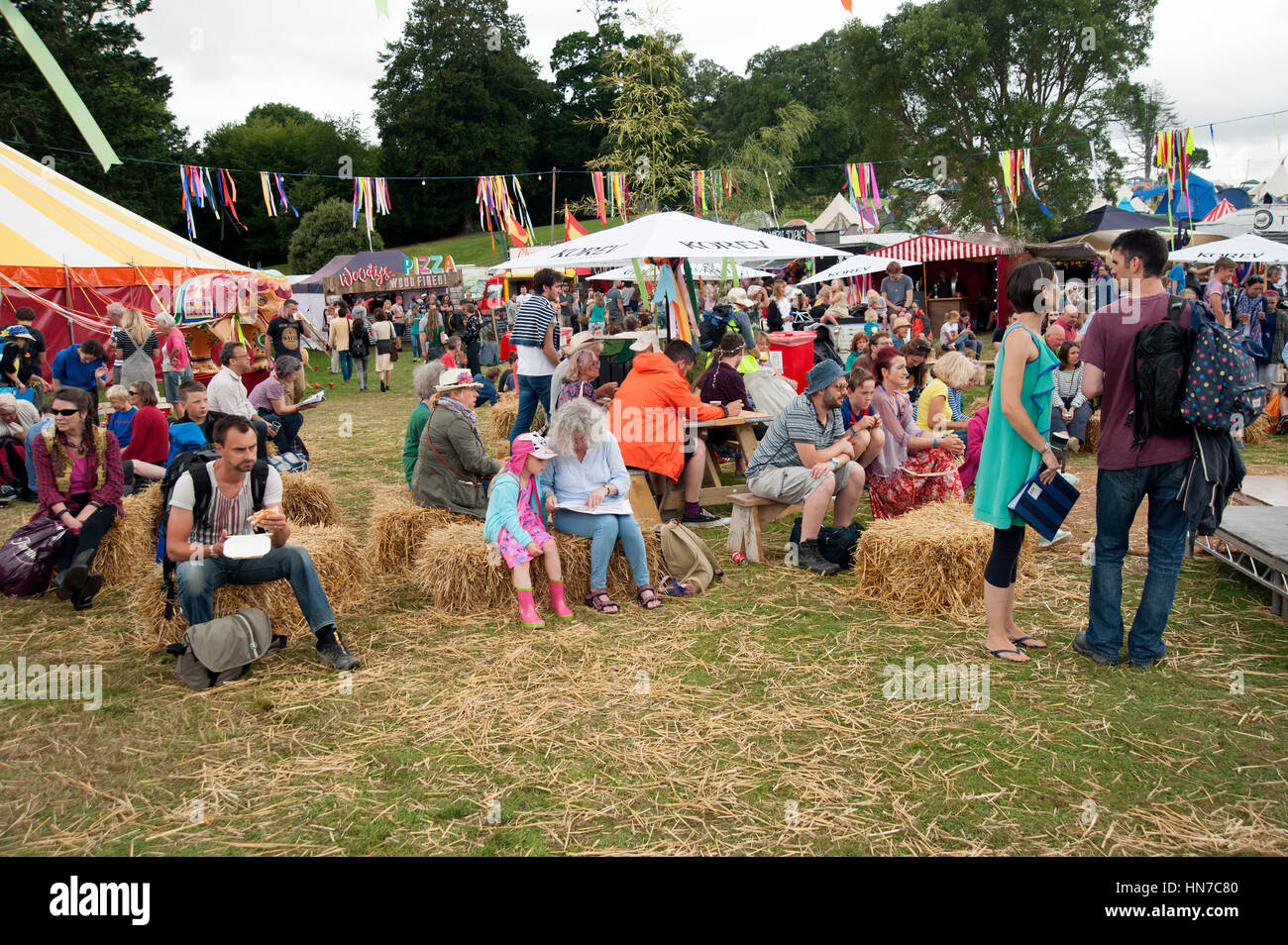 Familien, die auf Heuballen am Imbissstand sitzen und beim Port Eliot Festival Cornwall etwas trinken und essen Stockfoto