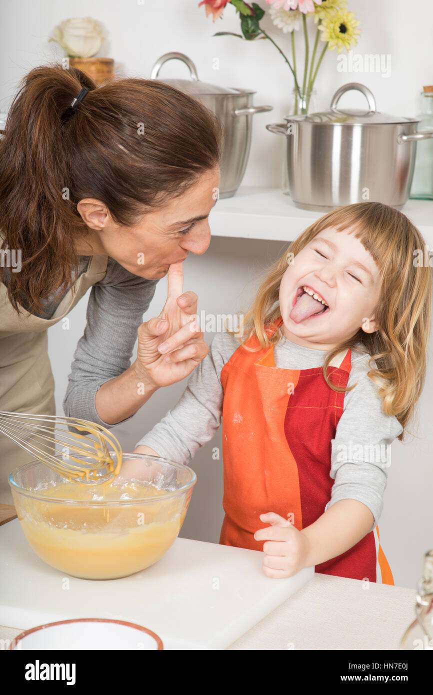 drei Jahre alt Schlagsahne Kind Lachen und Zunge mit Mutter saugen ihre Finger nach Belieben herausnehmen, in Teamarbeit, Kochen ein Biskuit bei kitc Stockfoto