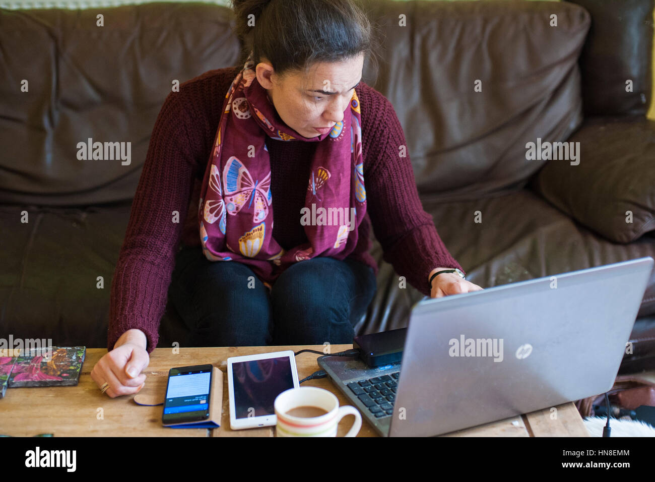 Arbeiten von zu Hause aus UK Coronavirus lockten Selbstisolation ab. Frau in ihren dreißiger Jahren, die von zu Hause aus mit einem Laptop, Mobiltelefon und Tablet auf dem Kaffeetisch arbeitet Stockfoto