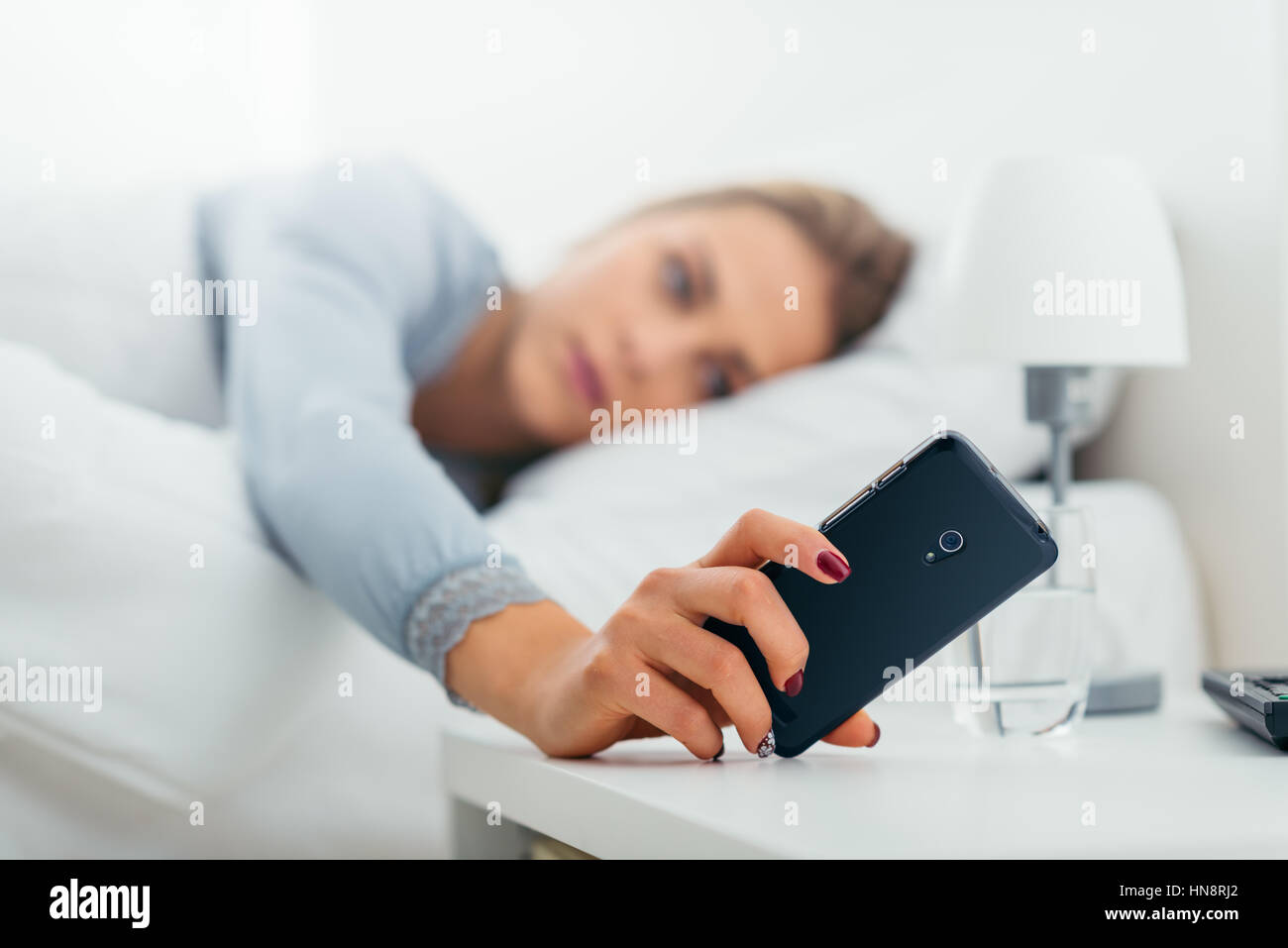 Junge Frau in ihrem Bett aufwachen und überprüft ihr Telefon Stockfoto