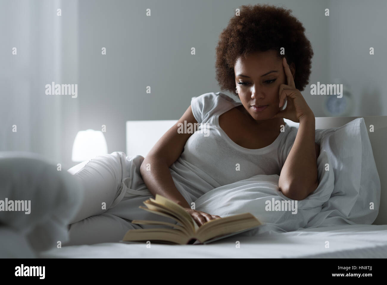 Schöne Frau auf dem Bett liegend, in der Nacht, sie ist im Bett liegen und lesen eine Buch, Lifestyle und Entspannung Konzept Stockfoto