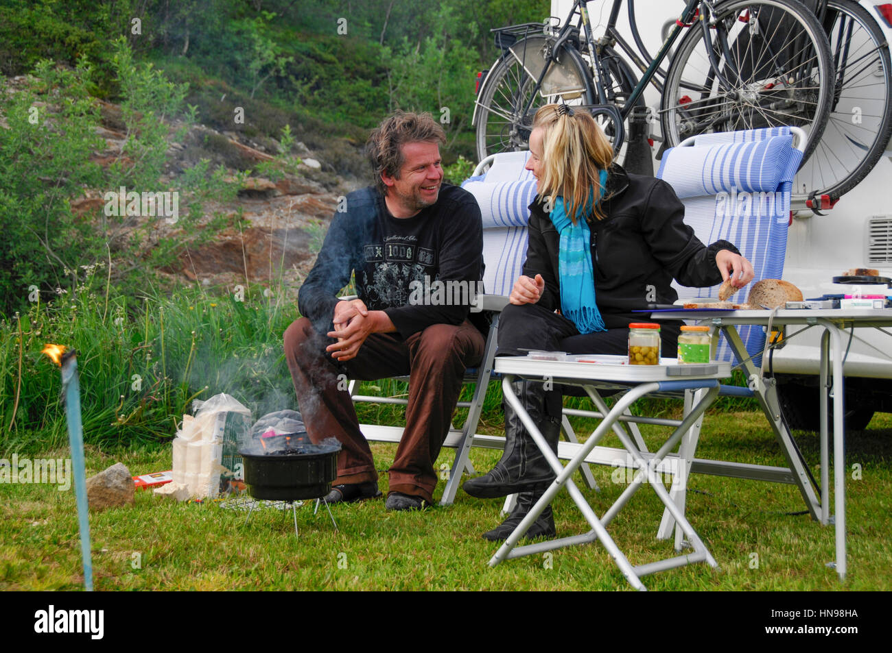 zu zweit im camping Stühle vor ihrem Wohnmobil sitzen und sie kochen auf dem Grill Stockfoto