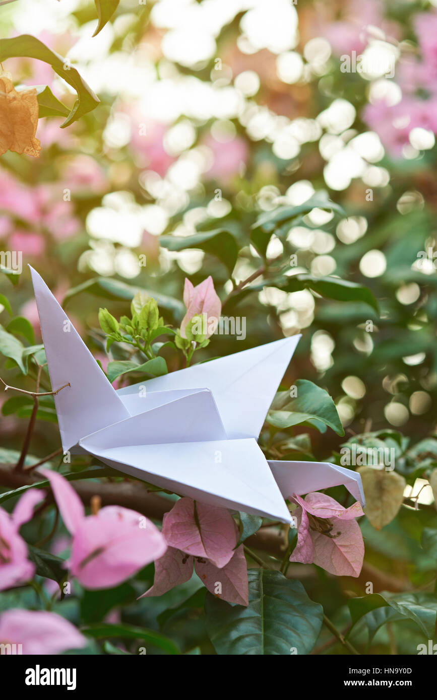 weiße Handwerk Papier Kran Aufenthalt auf rosa Garten Blumen Hintergrund Stockfoto