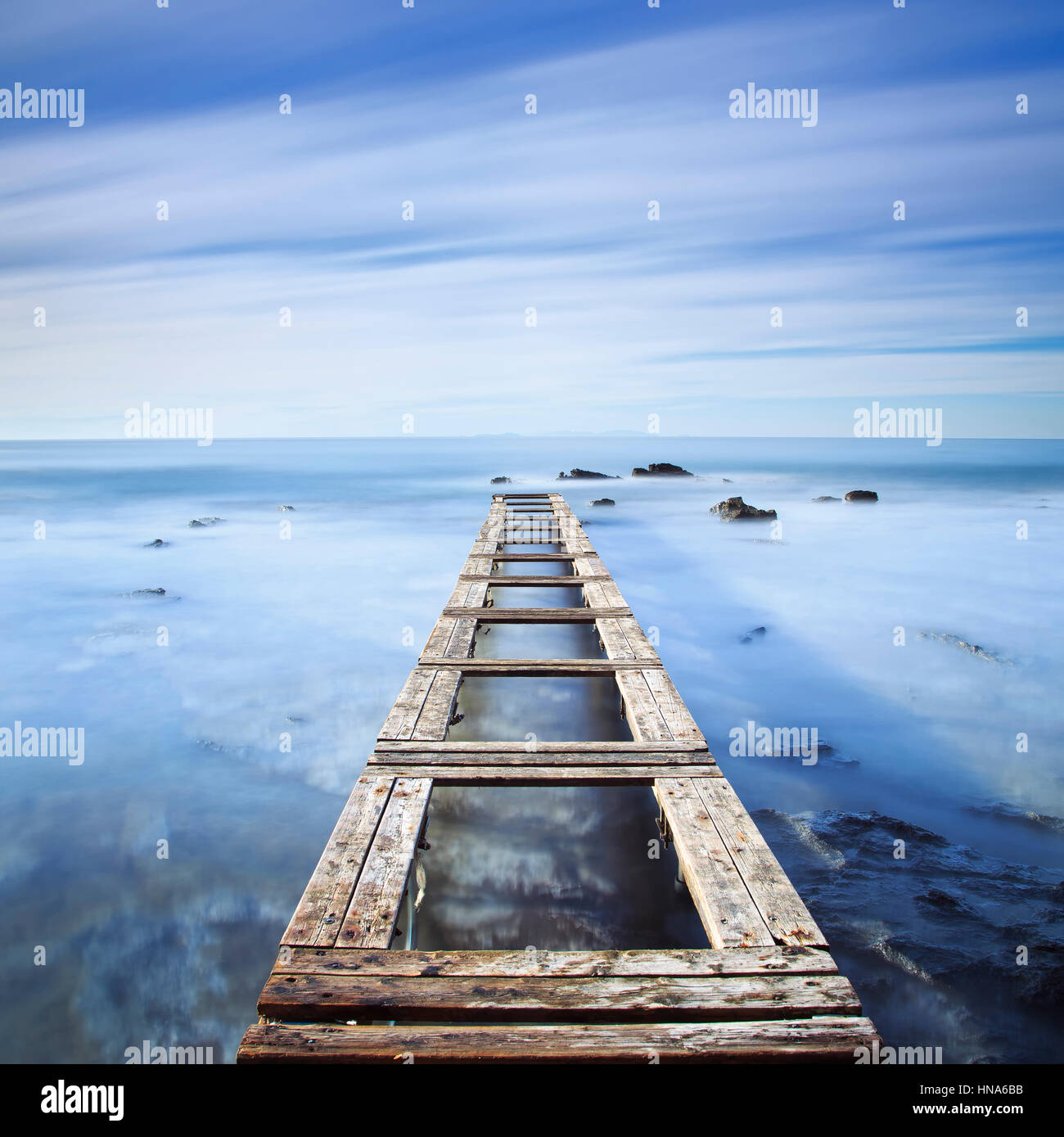 Hölzerne Pier oder Steg und Felsen auf einem blauen Ozean am Morgen. Langzeitbelichtung Stockfoto