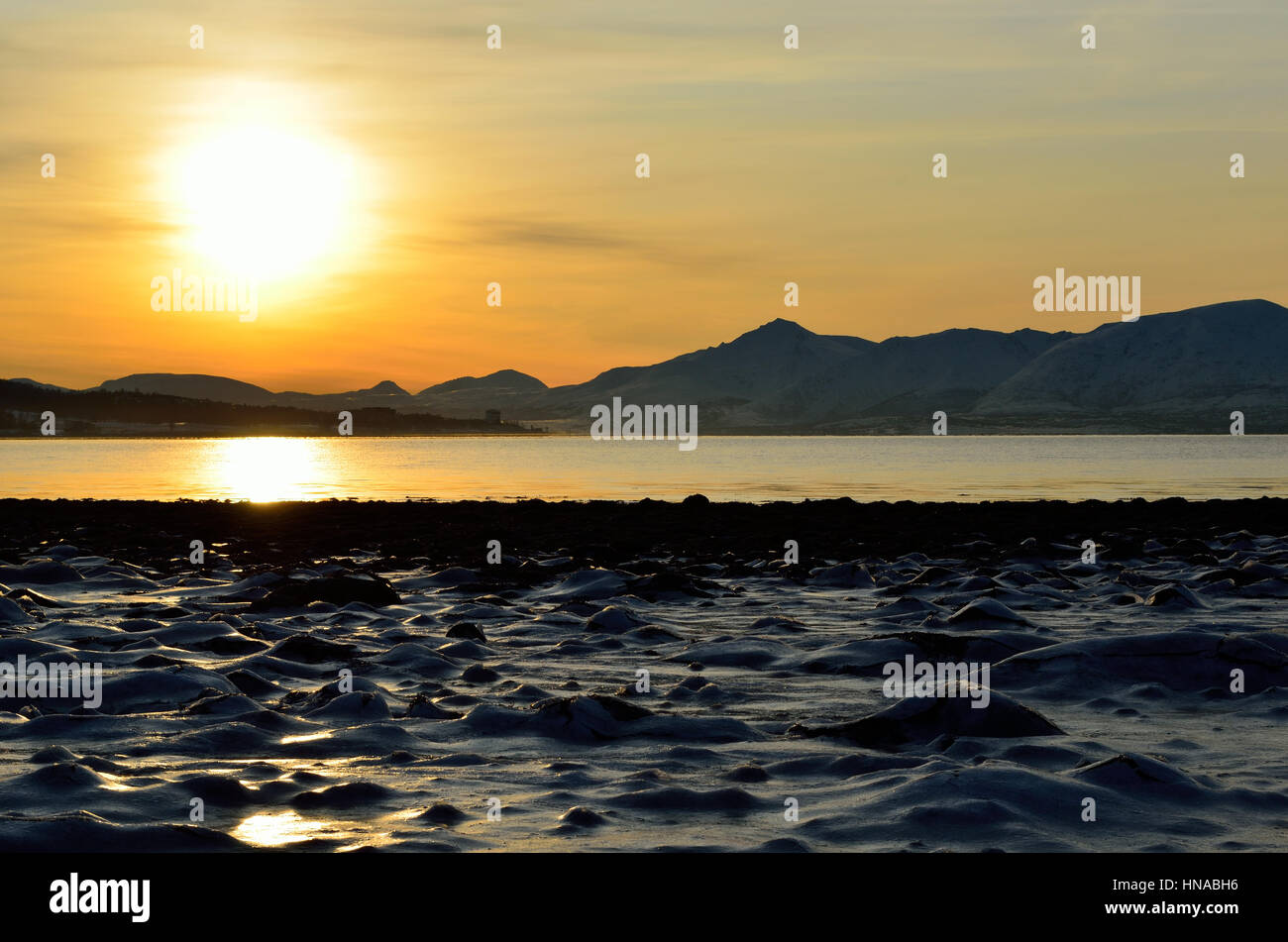 goldenen Sonnenaufgang über dem blauen Fjord und verschneiten Bergen mit Reflexion über dicken gefrorenen Meereis Ufer Stockfoto