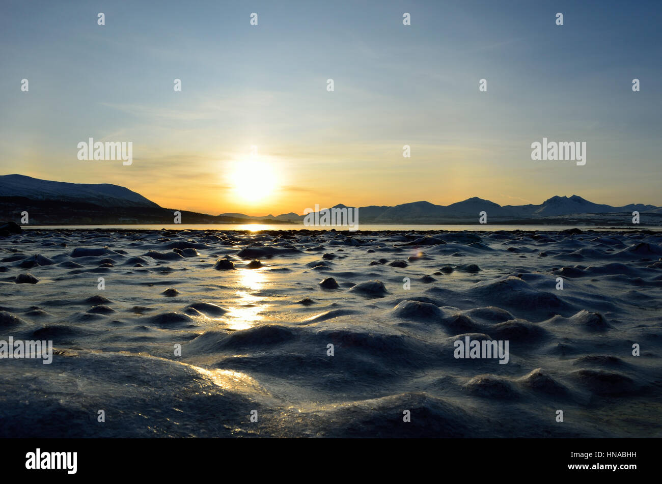 goldenen Sonnenaufgang über dem blauen Fjord und verschneiten Bergen mit Reflexion über dicken gefrorenen Meereis Ufer Stockfoto