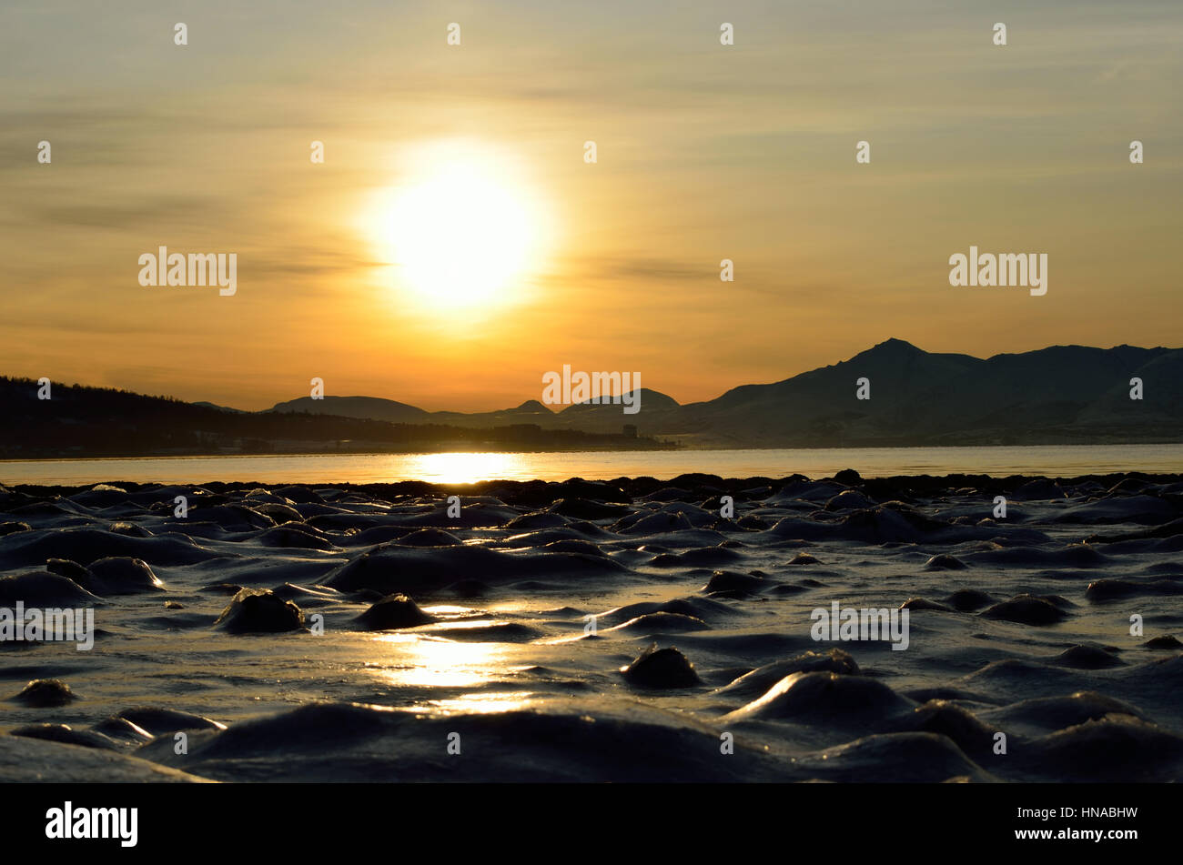 goldenen Sonnenaufgang über dem blauen Fjord und verschneiten Bergen mit Reflexion über dicken gefrorenen Meereis Ufer Stockfoto