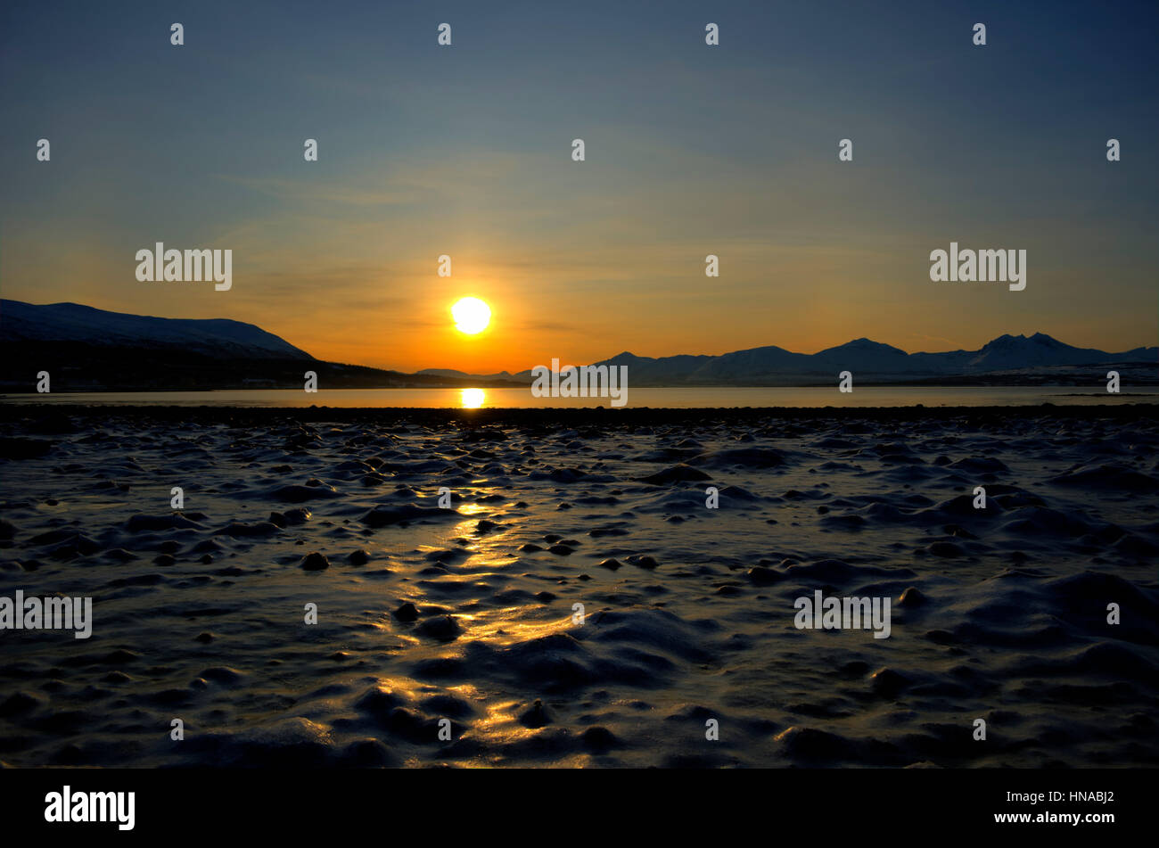 tief lebendigen goldener Sonnenaufgang über dem Fjord und verschneiten Berglandschaft mit Reflexion am festen gefrorenen Meer Stockfoto