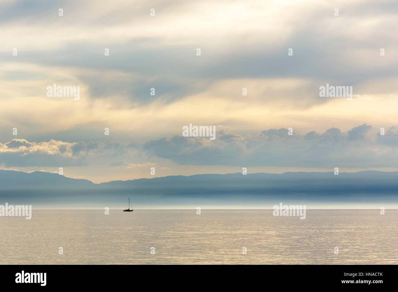 Silhouette der Segelboote auf dem Wasser des Genfer Sees an einem nebligen Tag im Licht der Sonne, die langsam den Horizont nähert sieht in der di Stockfoto