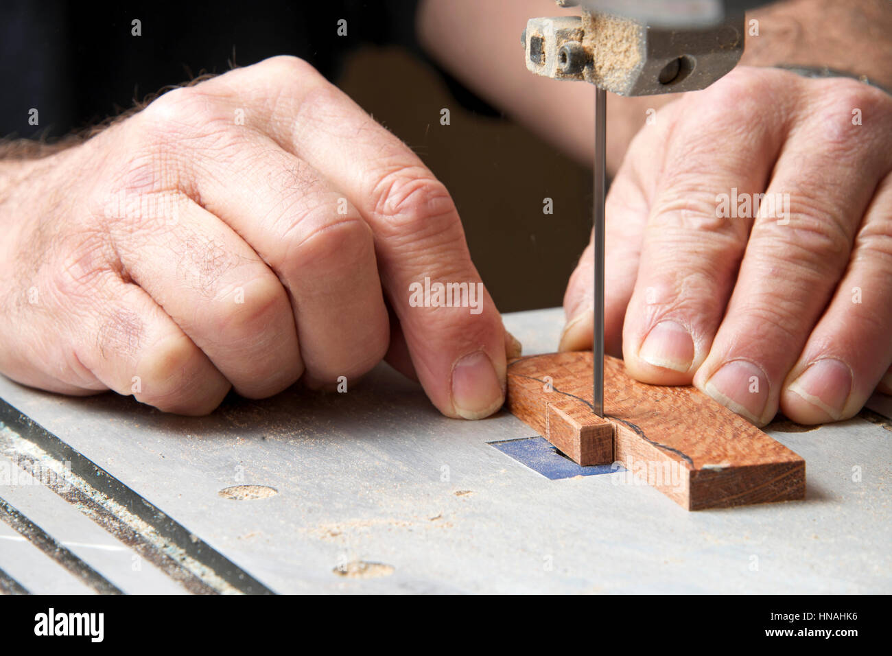 Männliche Hände halten ein kleines Stück Holz Präzisionsschneiden auf einer Tischplatte Jig sah. Sägespäne überall. Stockfoto