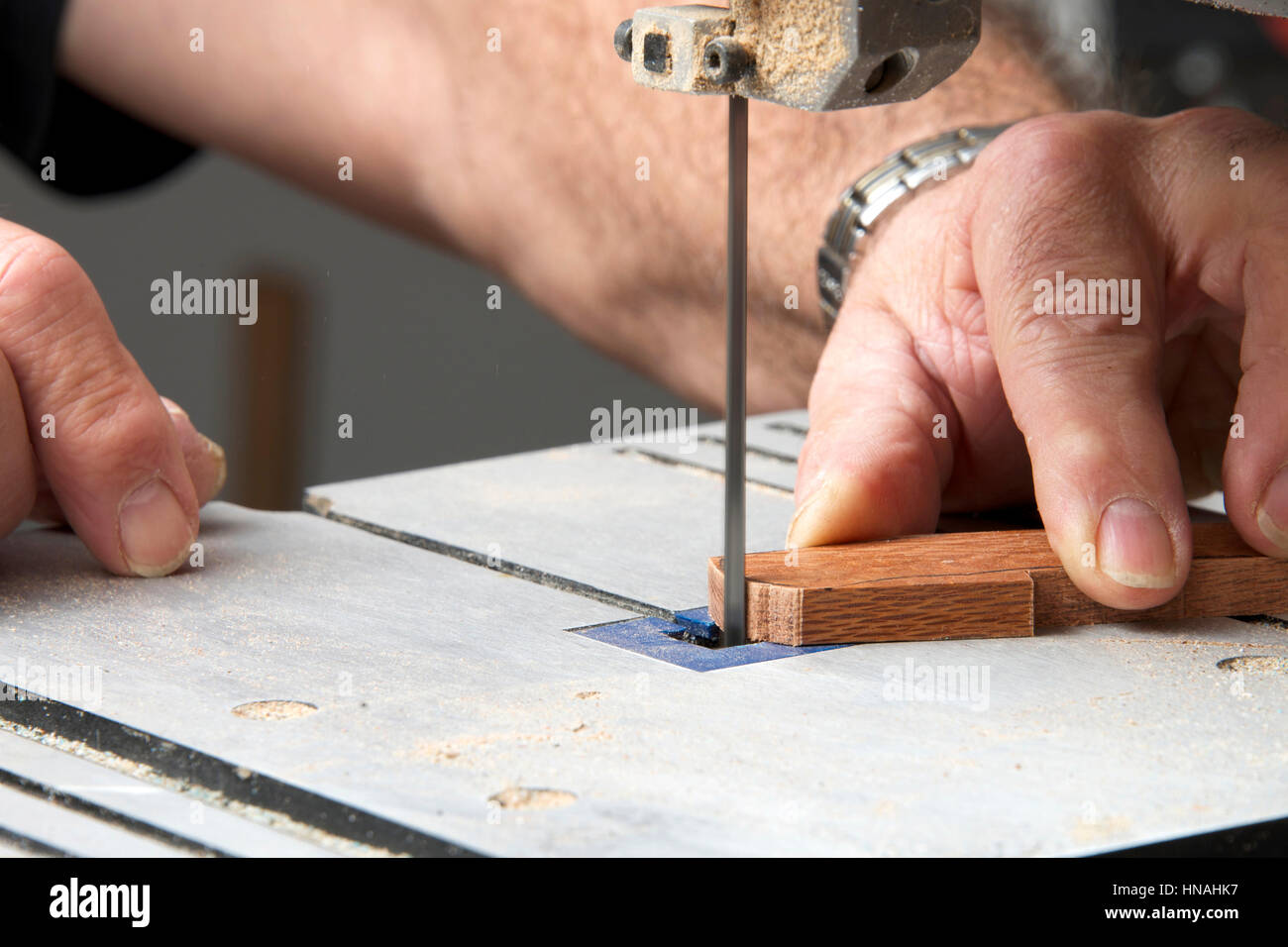 Männliche Hände halten ein kleines Stück Holz Präzisionsschneiden auf einer Tischplatte Jig sah. Sägespäne überall. Stockfoto