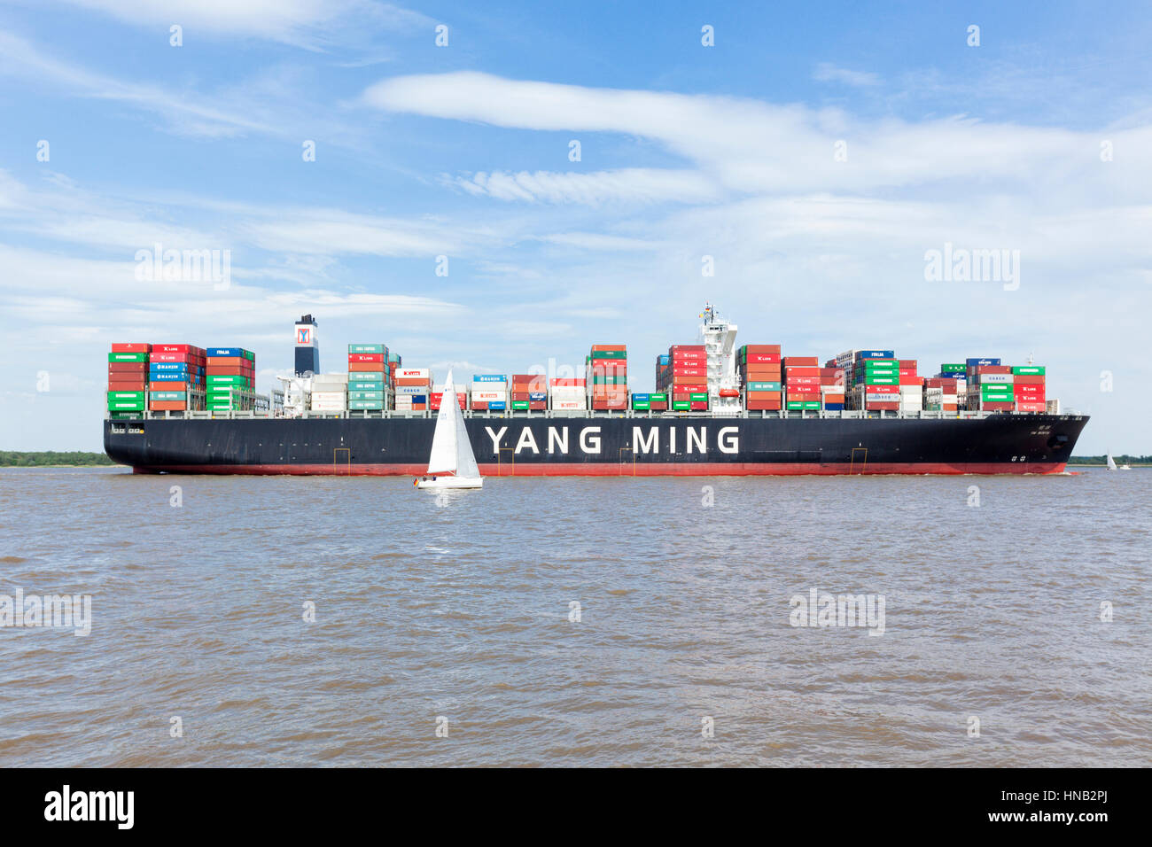 Stade, Deutschland - 22. Mai 2016: Ultra große Containerschiff YM Wert an der Elbe in der Nähe von Hamburg, ein kleines Segelboot vorbei. YM Wert kann 14,0 halten Stockfoto