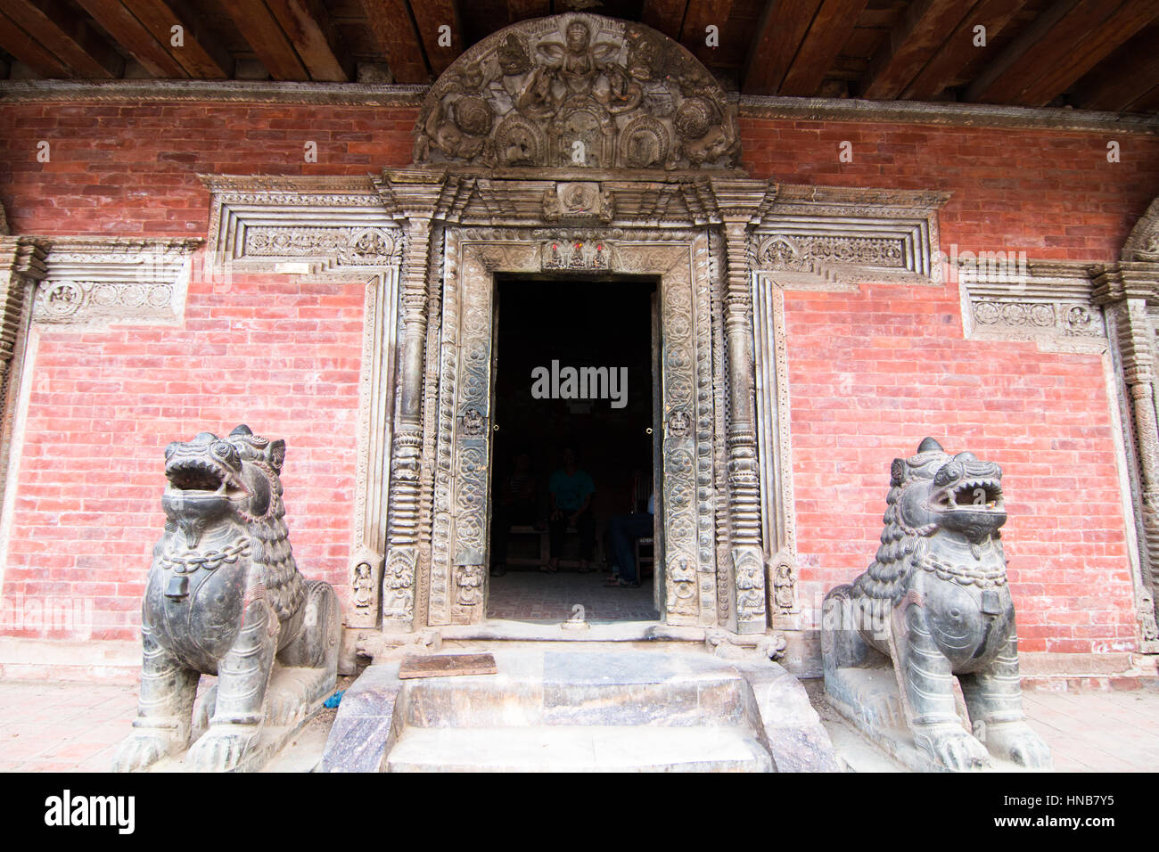 Löwen bewachen den Eingang am Eingang eines alten Gebäudes mit einer kunstvoll geschnitzten hölzernen Türsturz in Bhaktapur, Kathmandu, Nepal Stockfoto