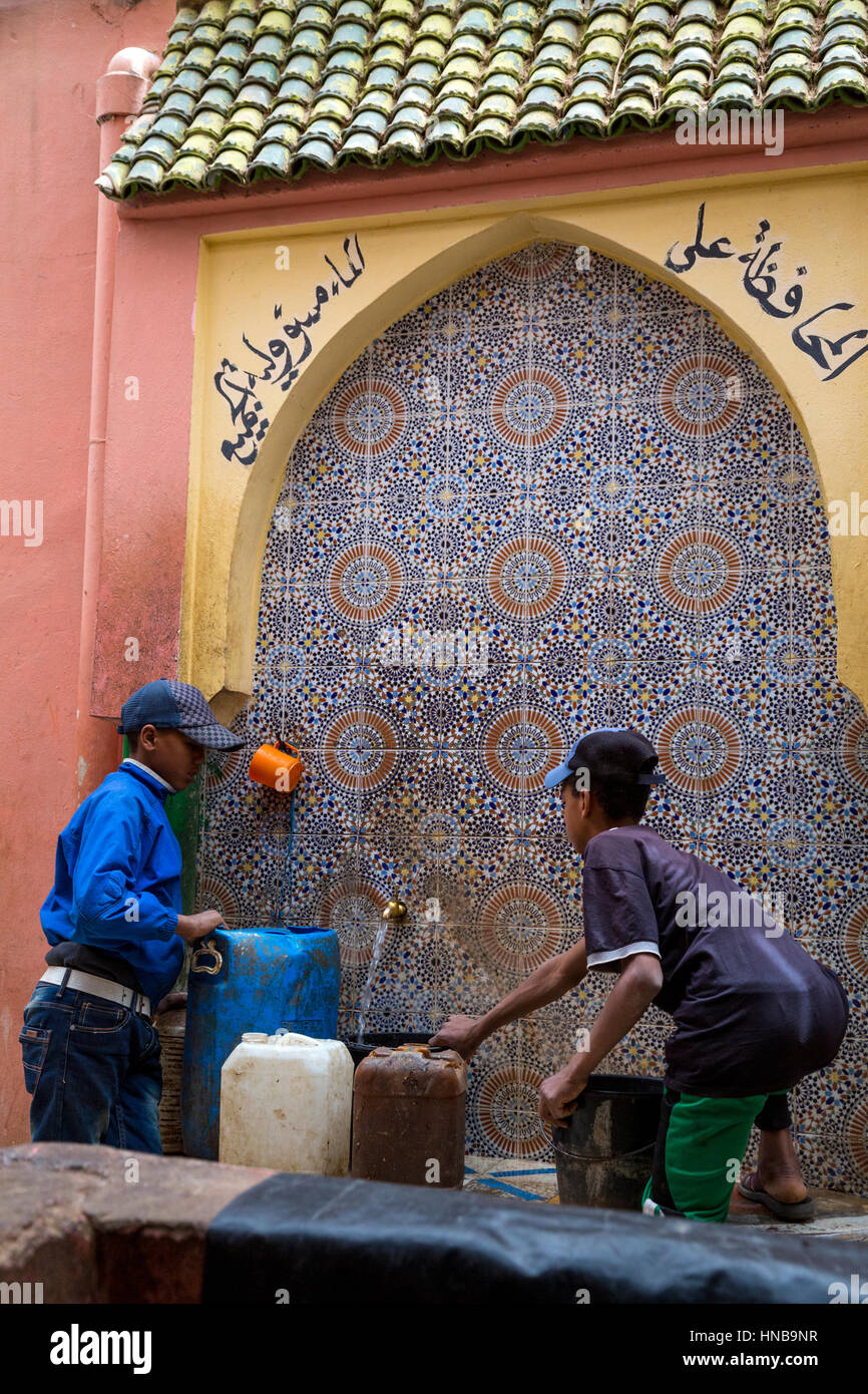 Rissani, Marokko.  Jungen füllen Wasser Krüge an die Öffentlichkeit Wasserhahn auf dem Markt.  Das arabische sagt "Wassersparen ist jedermanns Verantwortung." Stockfoto