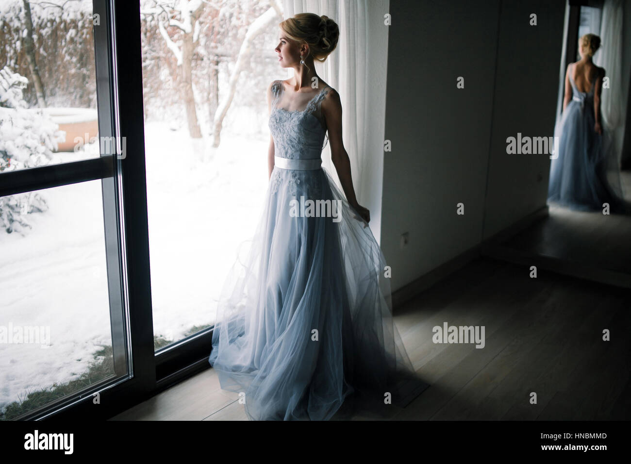 Braut, stehen vor großen Fenster und blickte zum verschneiten Garten. Ihre Figur spiegelt sich in den großen Spiegel. Stockfoto