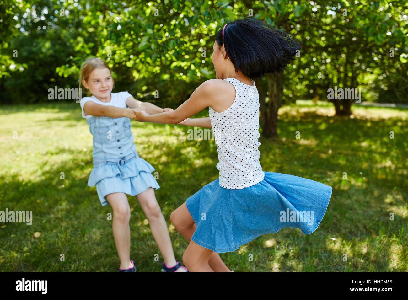 Zwei aktive Mädchen herumtollen und im Sommer den Händen halten und Spaß haben Stockfoto