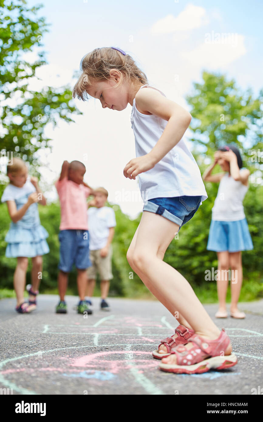 Mädchen springt mit Konzentration an Himmel und Hölle Spiel im Sommer Stockfoto