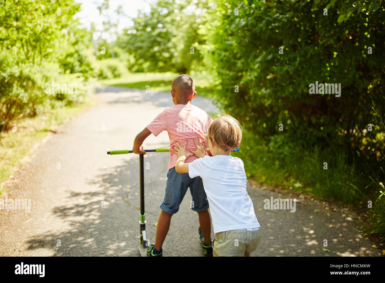 Zwei Kinder als Freunde spielen mit Scooter im Park im Sommer Stockfoto