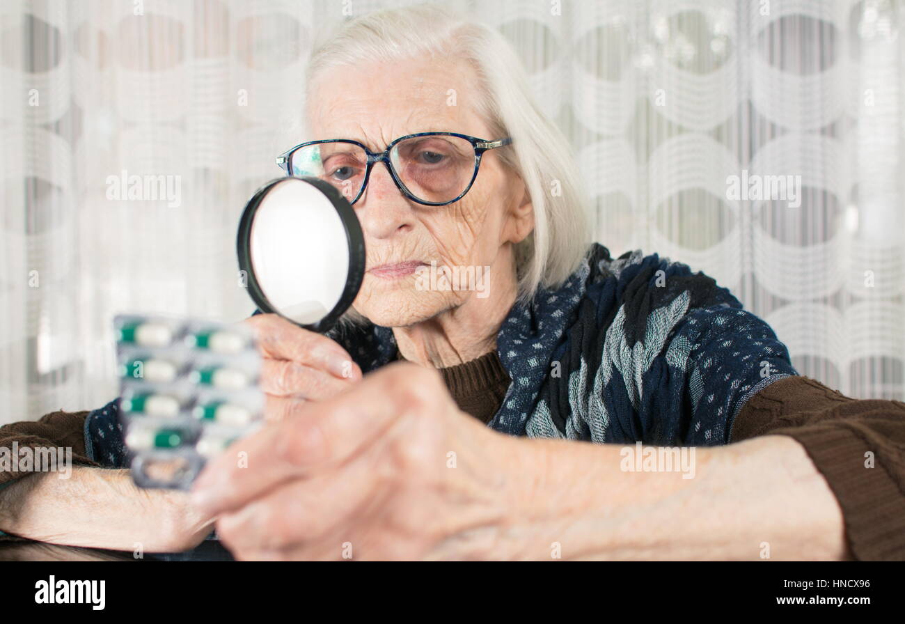 Ältere Frau liest Pille Namen mit Lupe zu Hause Stockfoto