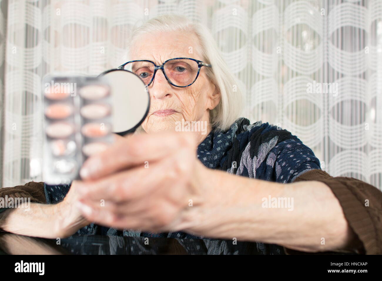 Ältere Frau liest Pille Namen mit Lupe zu Hause Stockfoto