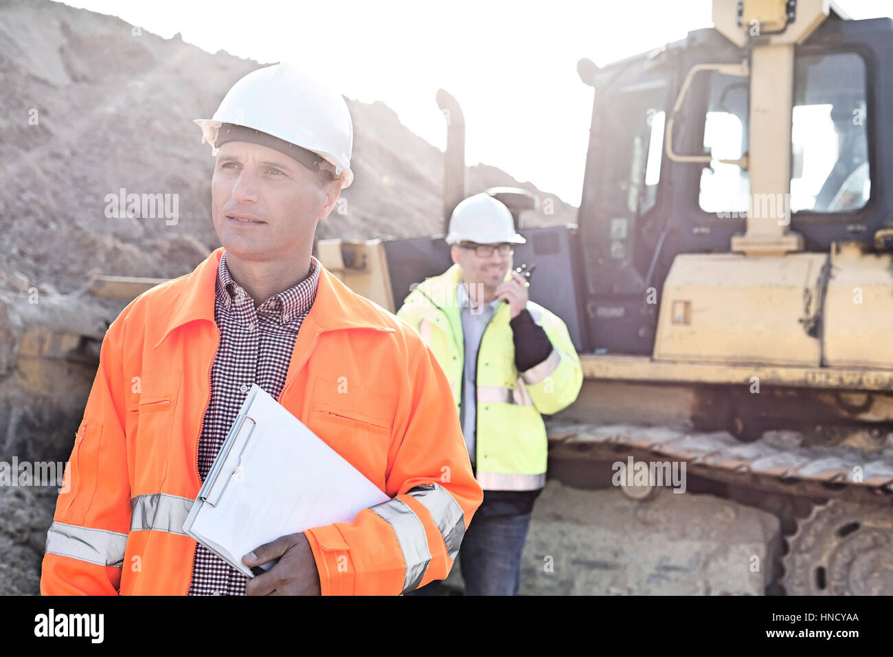 Ingenieur mit Zwischenablage auf Baustelle mit Kollegen im Hintergrund Stockfoto