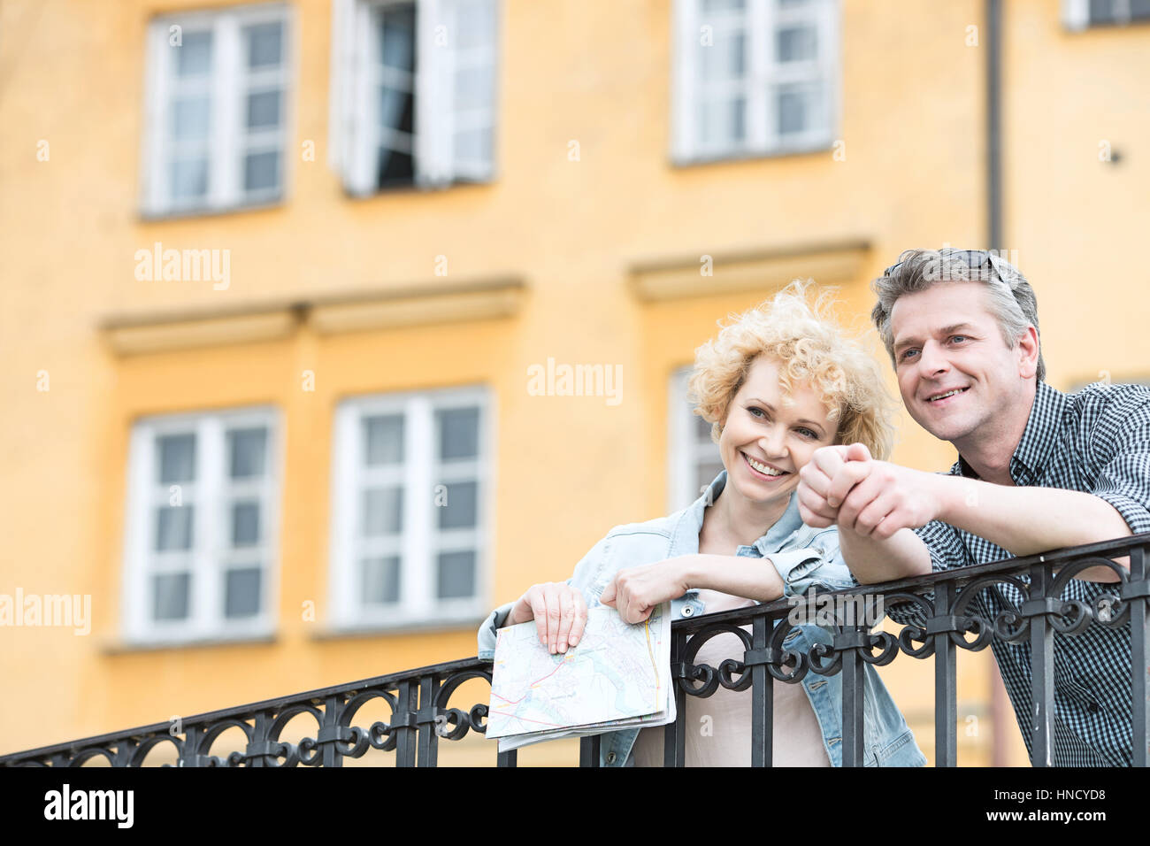 Glückliches Paar mittleren Alters mit Karte stützte sich auf Geländer gegen Gebäude Stockfoto