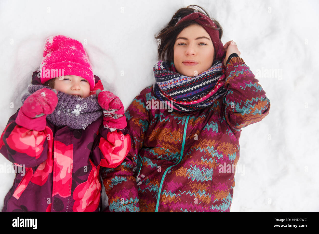 Frau mit Tochter tagsüber auf Schnee im Winter Park liegen Stockfoto