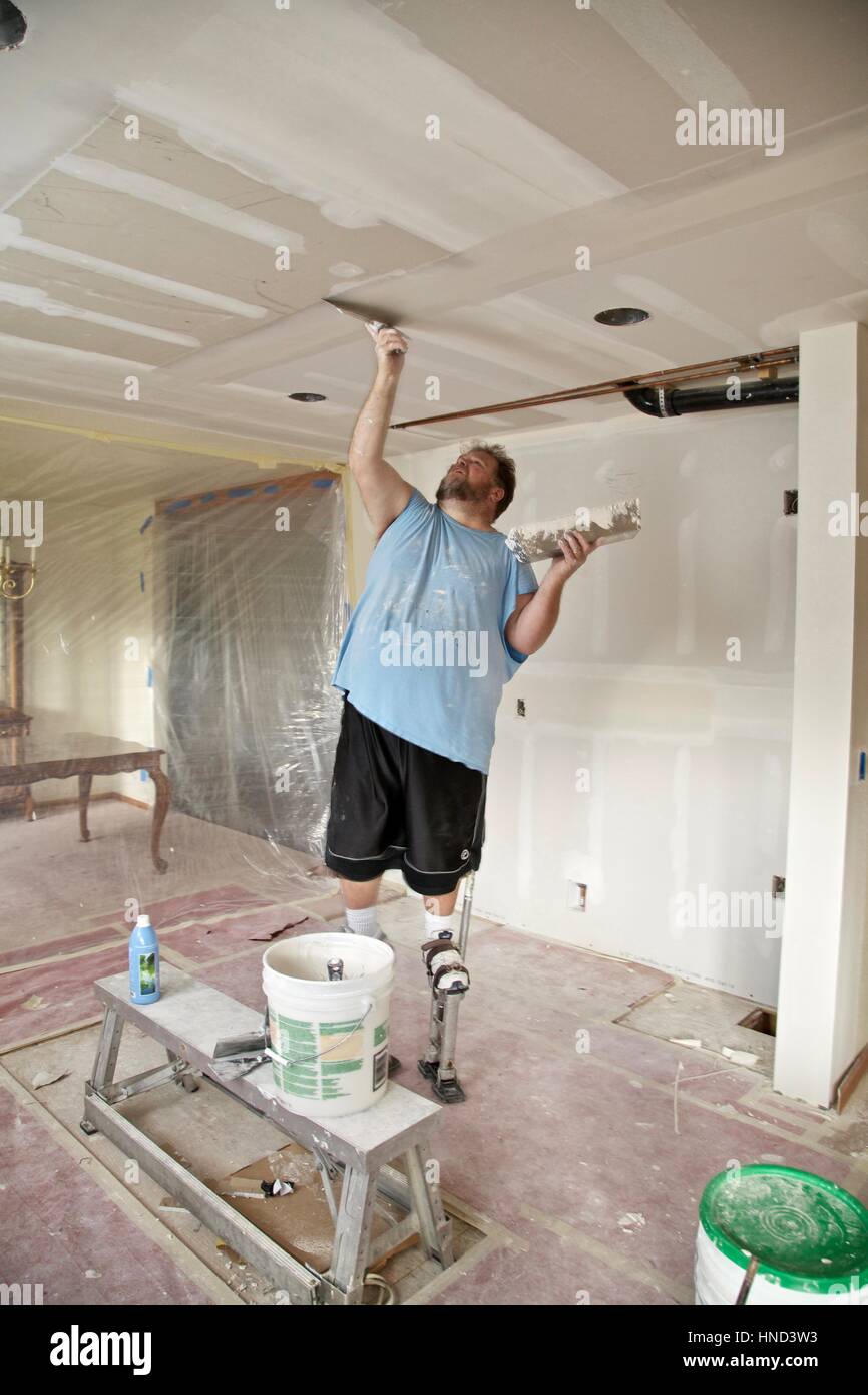 Ein Trockenbau-Finisher gilt funkelnden Verbindung zur Decke Gelenke auf Stelzen stehend. Stockfoto