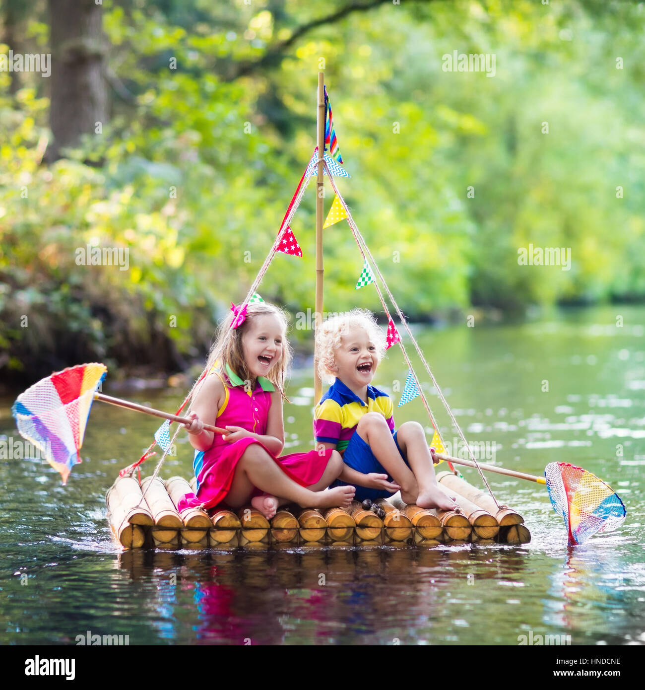 Zwei Kinder auf hölzerne Floß Fang von Fischen mit einem bunten Netz in einem Fluss und das Spiel mit Wasser am heißen Sommertag. Outdoor-Spaß und Abenteuer für Kinder. Stockfoto