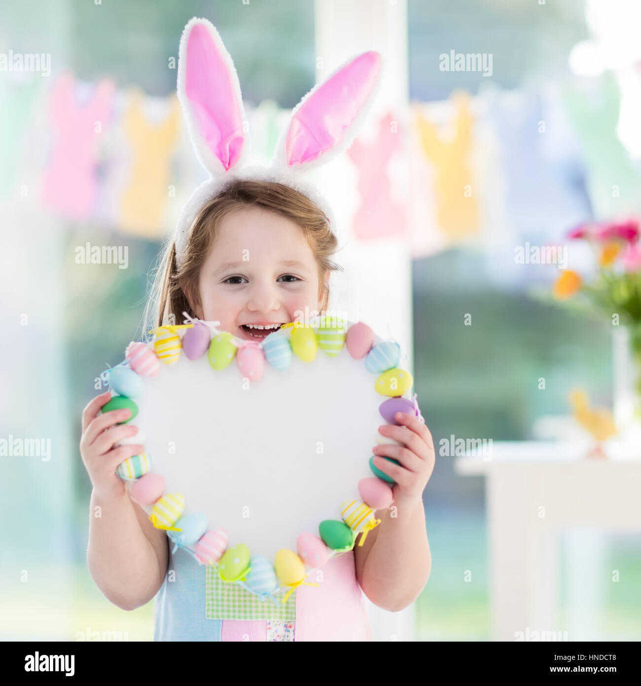 Glückliche kleine Mädchen in Hasenohren hält ein Herz-Board mit bunten Ostereiern. Kinder feiern Ostern. Kinder, die Spaß auf Ostereiersuche. Pastell Stockfoto