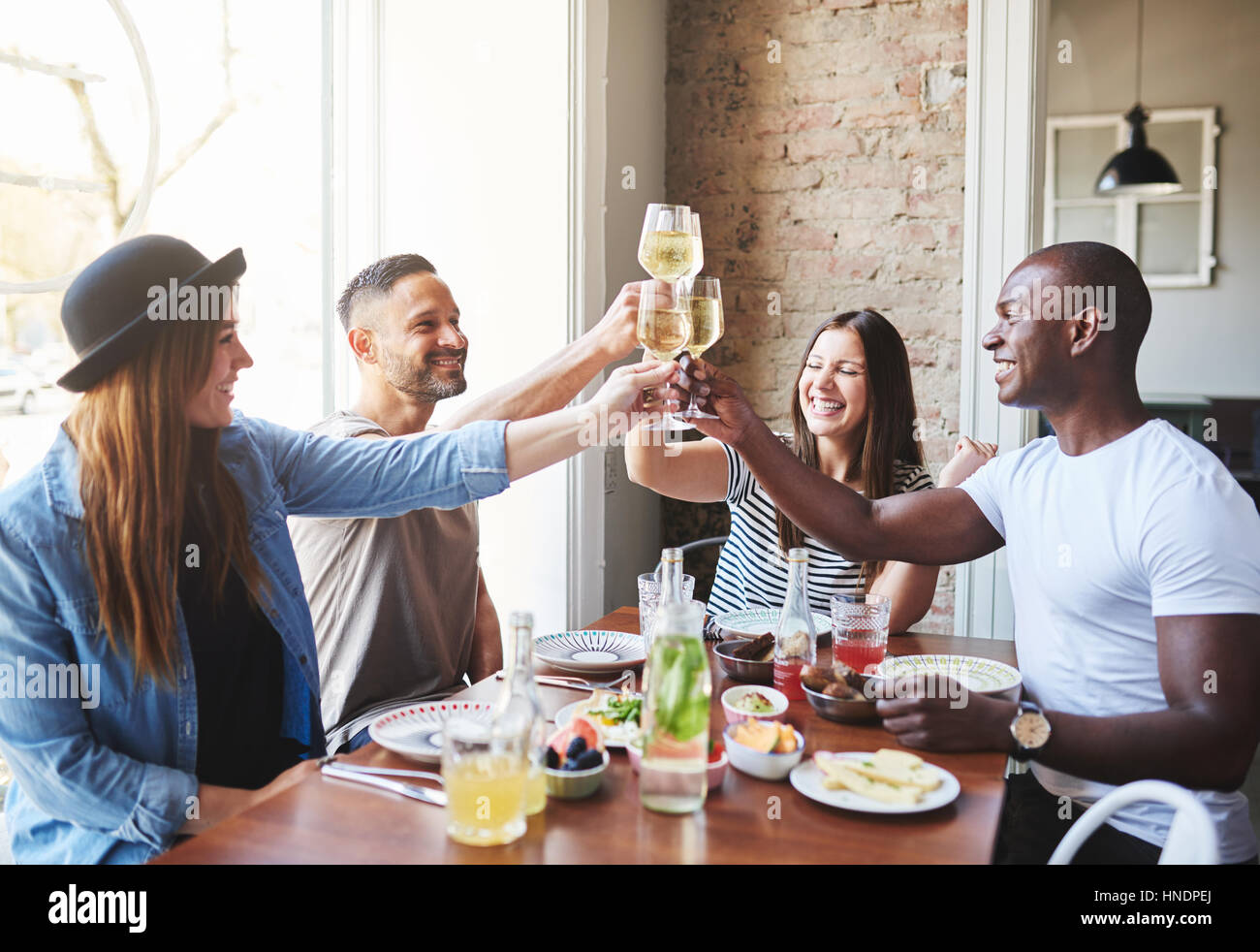 Vier junge Erwachsene sitzen am Tisch und klirrende Gläser Wein beim Abendessen gemeinsam im Restaurant. Stockfoto