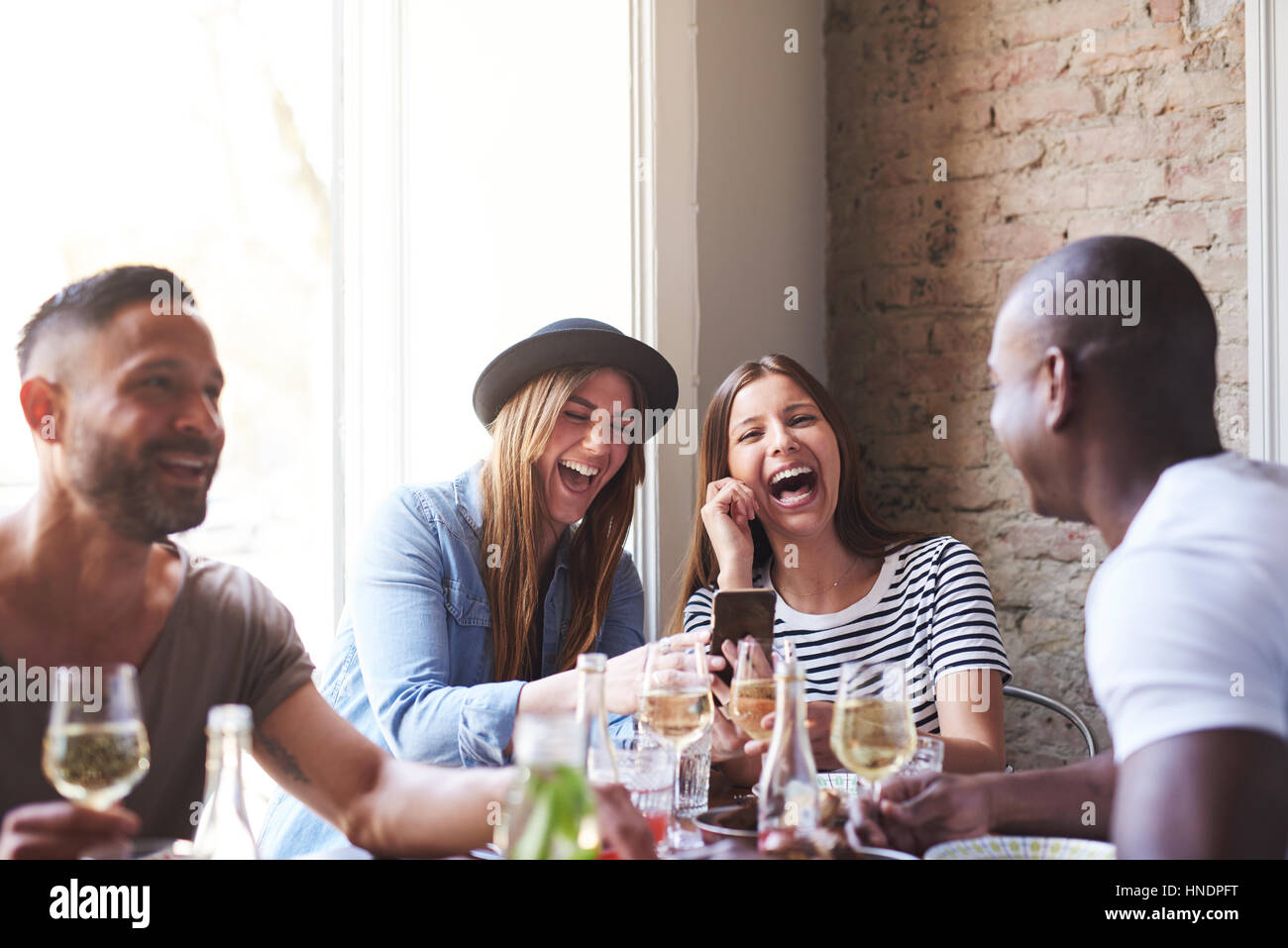 Kleine Gruppe von vier unterschiedlichen Freunde lachten etwas auf Handy am Tisch im restaurant Stockfoto