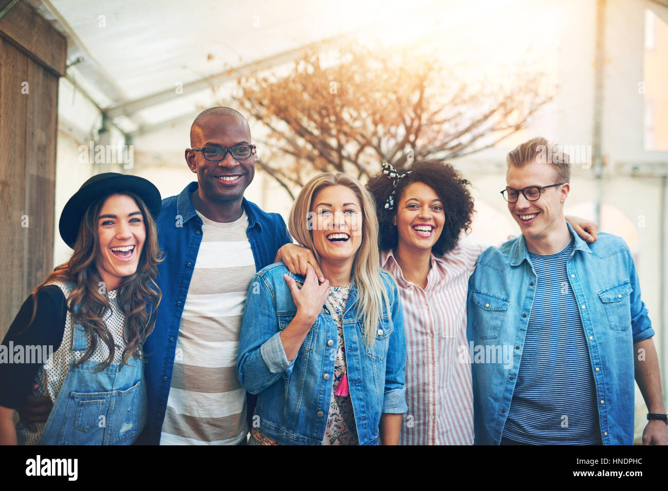 Gruppe von fünf schöne junge Menschen in Freizeitkleidung drinnen eng zusammenstehen, lachen und Lächeln zu Kamera posieren, Stockfoto