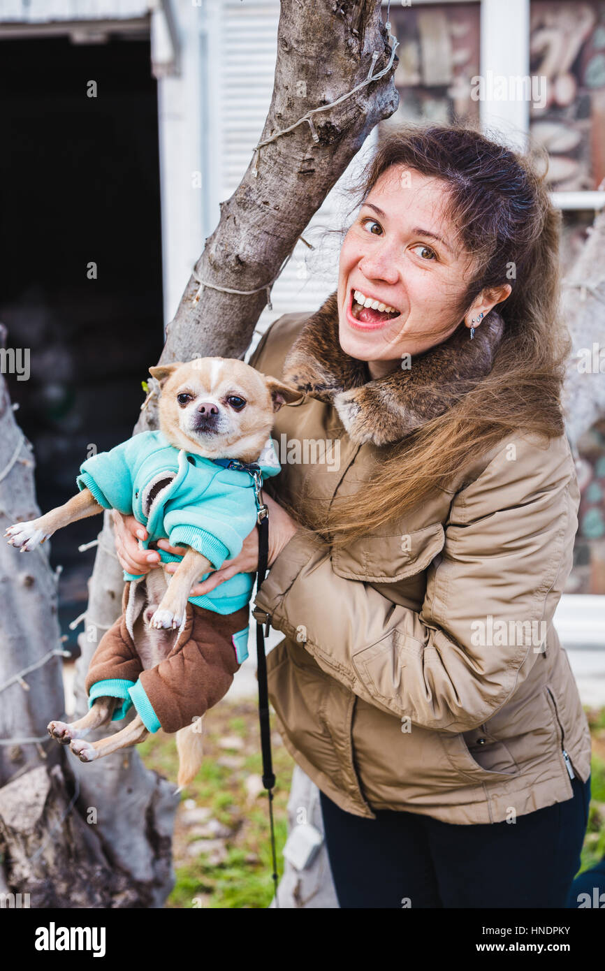 Porträt des jungen attraktiven lächelnd Brünette Frau ihre Hände im grüne Sommerpark kleine Chihuahua Hund festhalten. Stockfoto