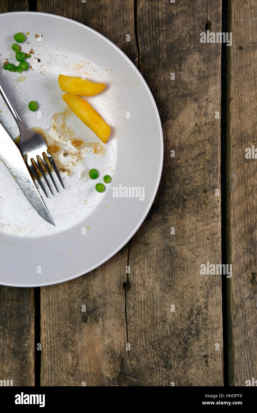 Draufsicht der Reste auf einem Teller mit Messer und Gabel auf einem rustikalen hölzernen Hintergrund Stockfoto