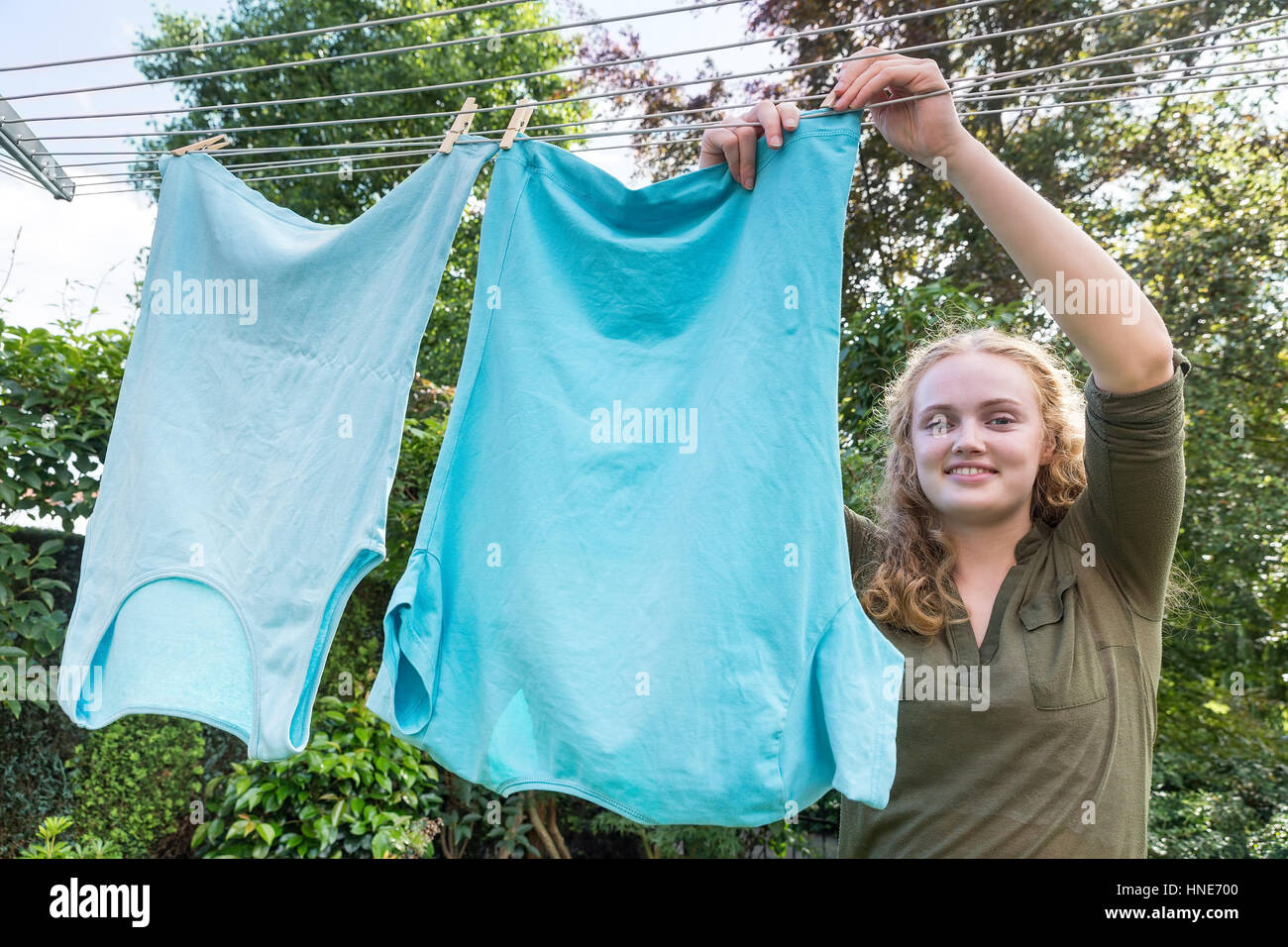 Kaukasischer Teenager-Mädchen hängt Kleidung auf der Wäscheleine draußen Stockfoto