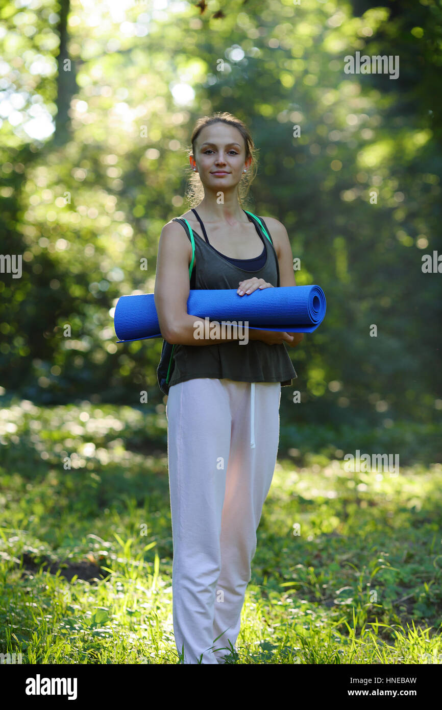 Junge Frau hält eine Yoga-Matte, stehend im Zauberwald Stockfoto