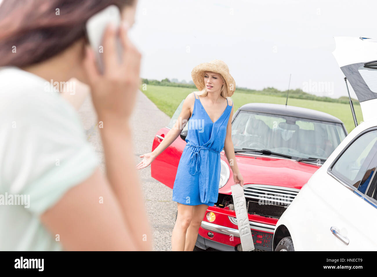 Böse Frau, die durch beschädigte Autos mit weiblichen mit Handy im Vordergrund Stockfoto