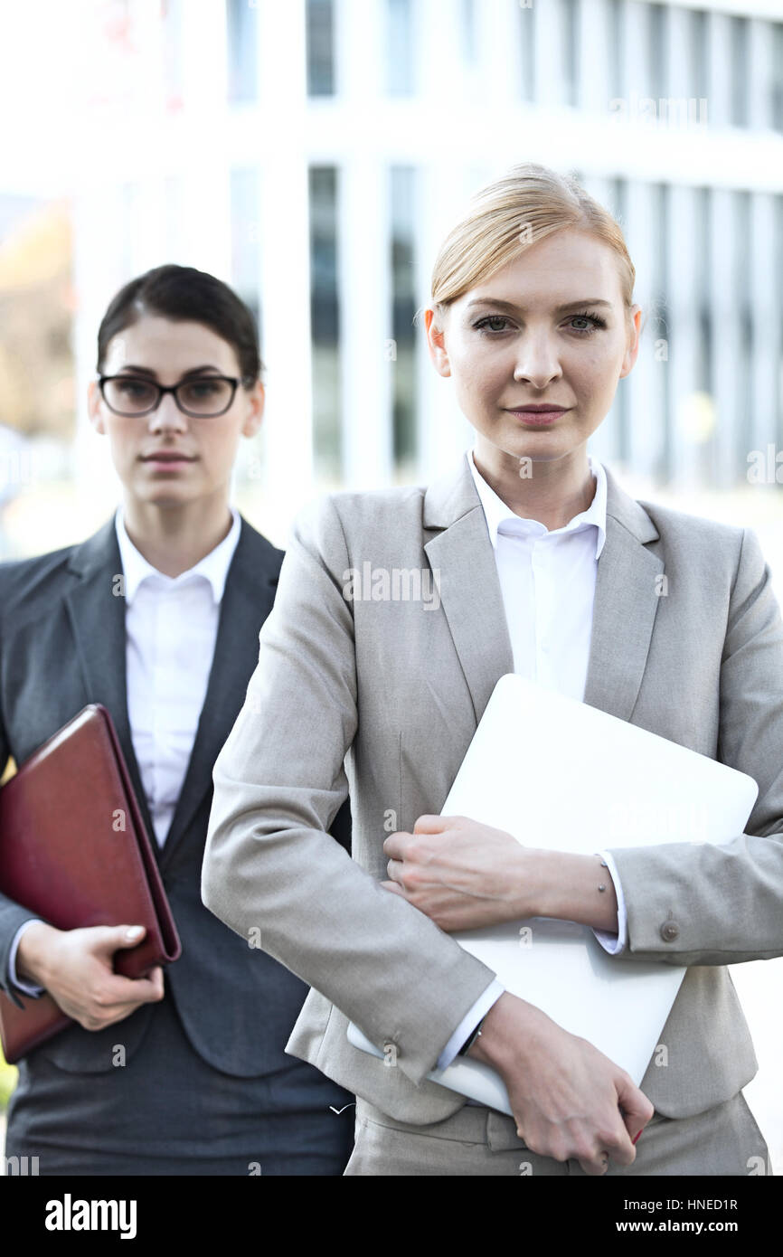 Porträt von zuversichtlich Geschäftsfrau hält Laptop mit Kollegen im Hintergrund Stockfoto