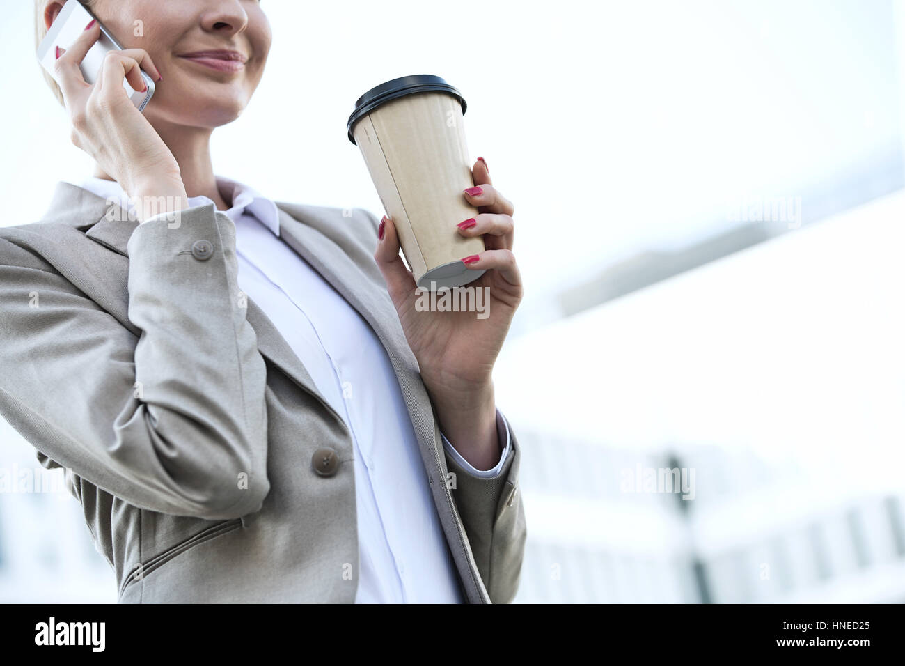 Mittelteil der Geschäftsfrau mit Handy halten Sie Einweg-Cup im freien Stockfoto