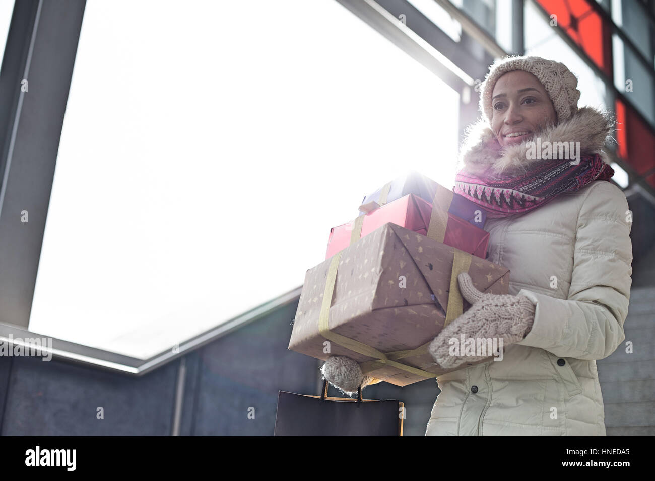 Lächelnde Frau in warme Kleidung tragen gestapelt Geschenke durch Fenster Stockfoto