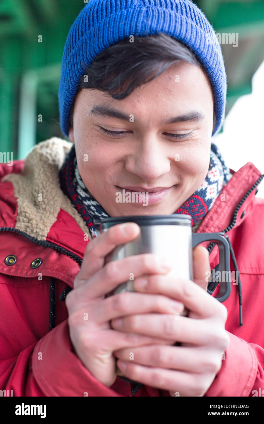 Lächelnder Mann betrachtet man Kaffee in isolierten Getränkeverpackung im winter Stockfoto