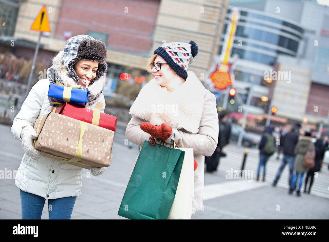 Glückliche Frauen mit Geschenken und Einkaufstaschen zu Fuß auf Stadtstraße im winter Stockfoto
