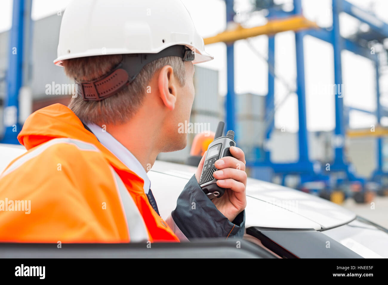 Mann mittleren Alters mit Walkie-talkie stehend neben Auto im Frachthafen Stockfoto