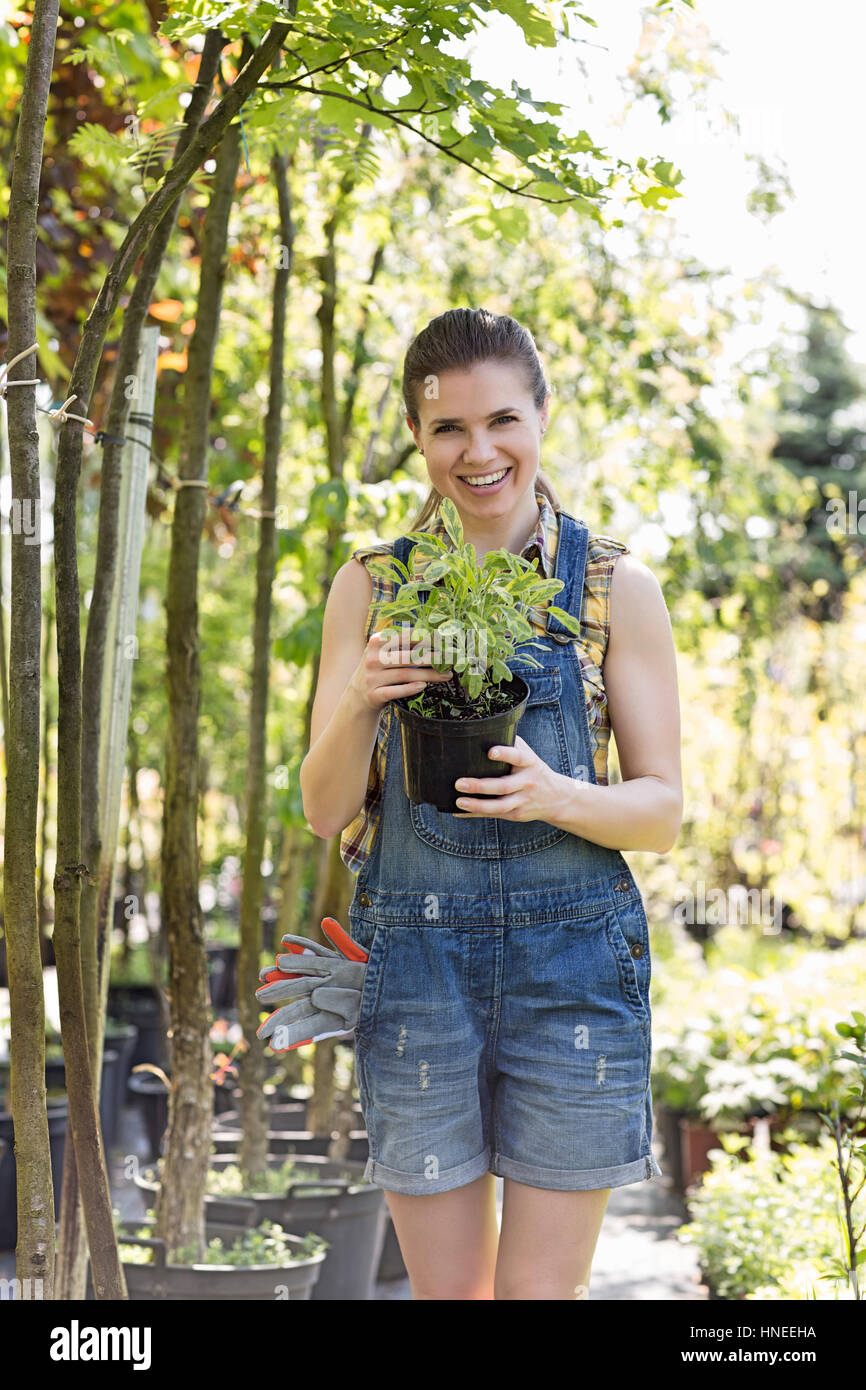 Porträt von glücklich Frau hält Topfpflanze im Garten Stockfoto
