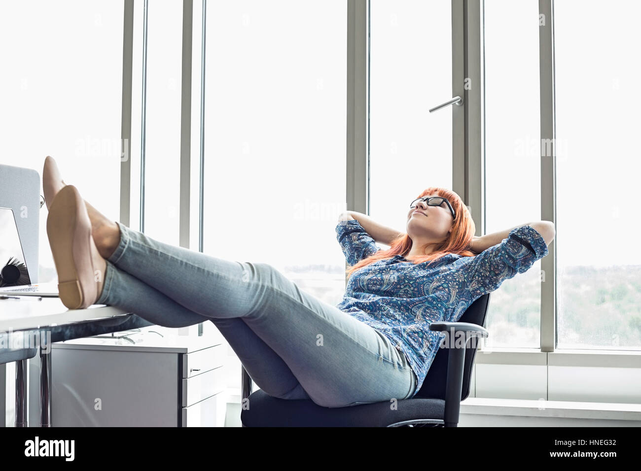 Der Geschäftsfrau entspannend mit Füße am Schreibtisch im Kreativbüro in voller Länge Stockfoto