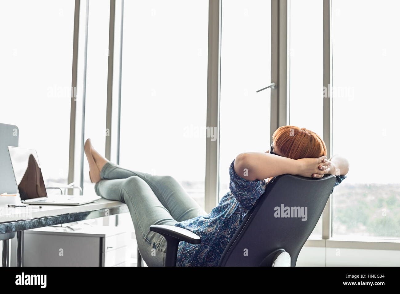 Seitenansicht der Geschäftsfrau entspannend mit Füße am Schreibtisch im Kreativbüro Stockfoto