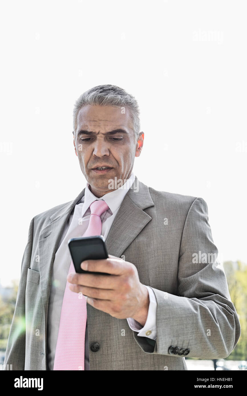 Geschäftsmann lesen SMS auf Handy gegen Himmel Stockfoto