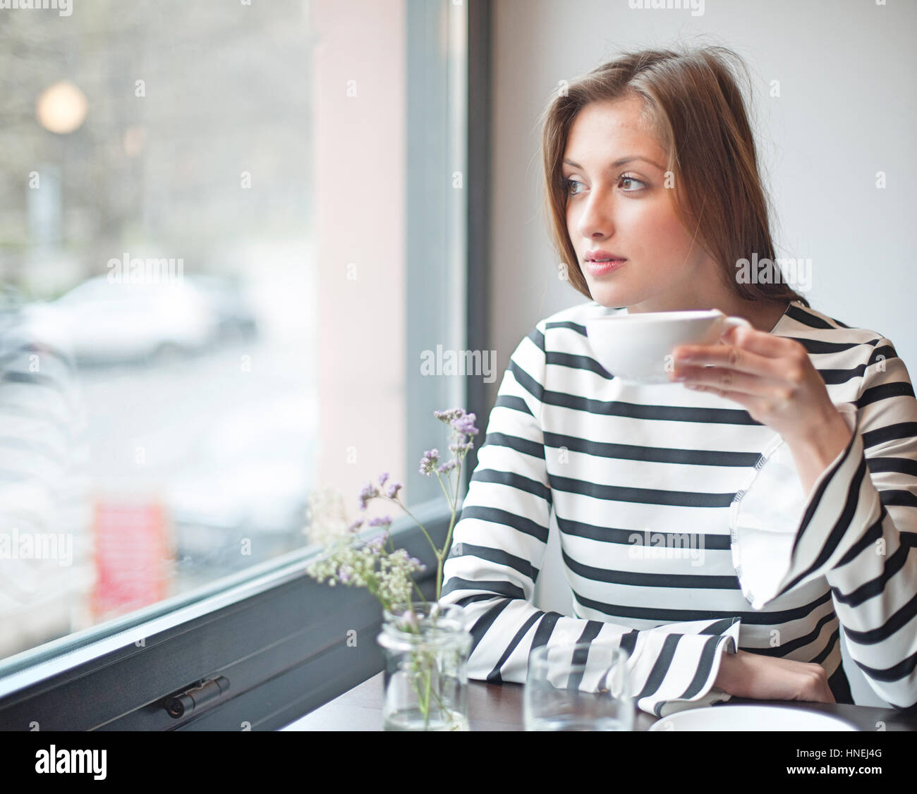 Nachdenkliche junge Frau mit Blick vom Fenster beim Kaffeetrinken im café Stockfoto