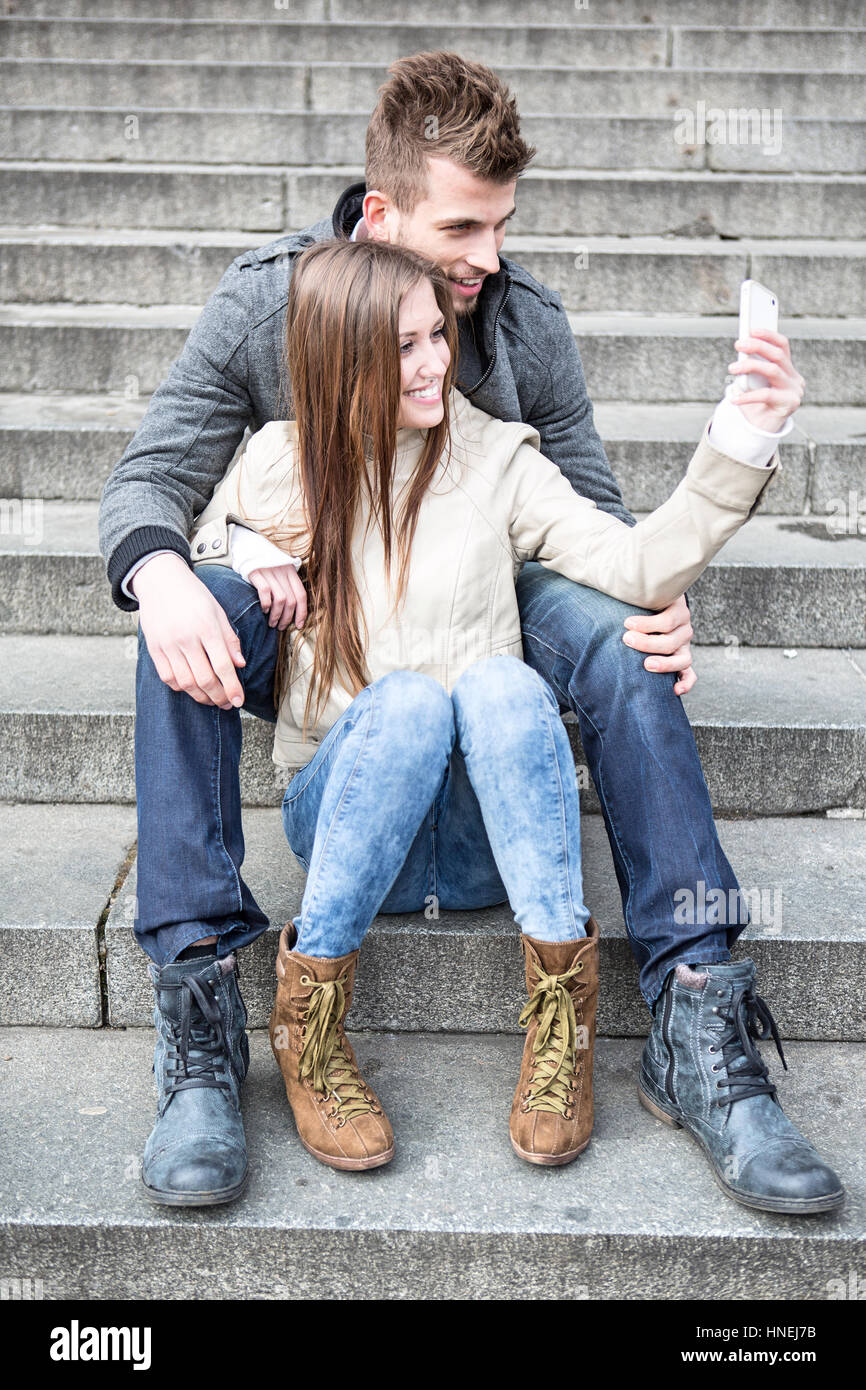 Volle Länge des jungen Paares unter Bild von sich selbst auf Schritte im freien sitzend Stockfoto